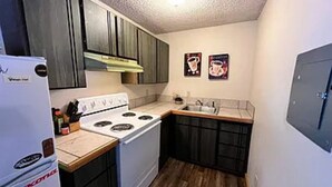 A compact kitchen with a white stove, dark wooden cabinets, and a small countertop. - Tiny cabin in the woods (Sandpoint)