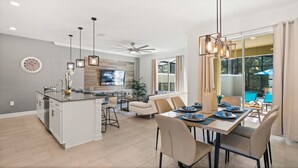 Une cuisine moderne dotée d’un îlot central, d’un coin repas avec une table pour quatre personnes et d’une grande fenêtre donnant sur une piscine.