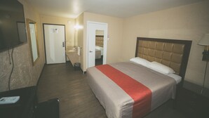Habitación de hotel con cama, escritorio, espejo y puerta que da a un baño.
