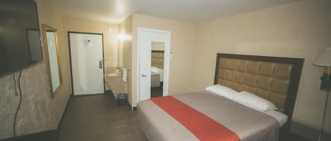 A hotel room with a bed, a desk, a mirror, and a door leading to a bathroom.