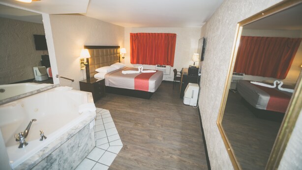 Habitación de hotel con una cama grande, una zona de estar independiente, un baño con bañera y un espejo que refleja la habitación.