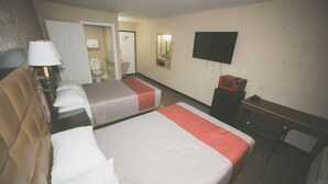 Habitación de hotel con dos camas, un escritorio, un televisor, un microondas y un baño visible a través de una puerta abierta.