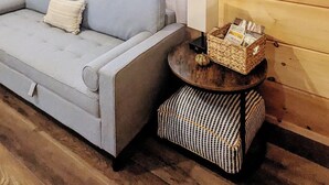 Interior acogedor de una cabaña con un sofá de color gris claro, una mesita redonda con una cesta y un cuadro de ciervos en la pared.