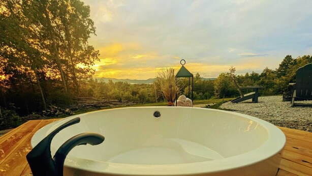 Un jacuzzi en una terraza de madera con vistas al atardecer.