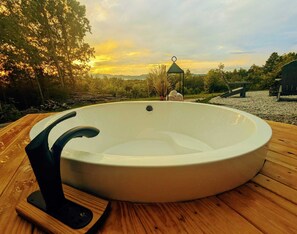 Un jacuzzi en una terraza de madera con vistas al atardecer.
