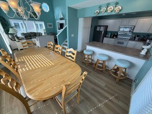 A dining area with a wooden table and chairs, a kitchen with white cabinets, and a staircase leading to another level.