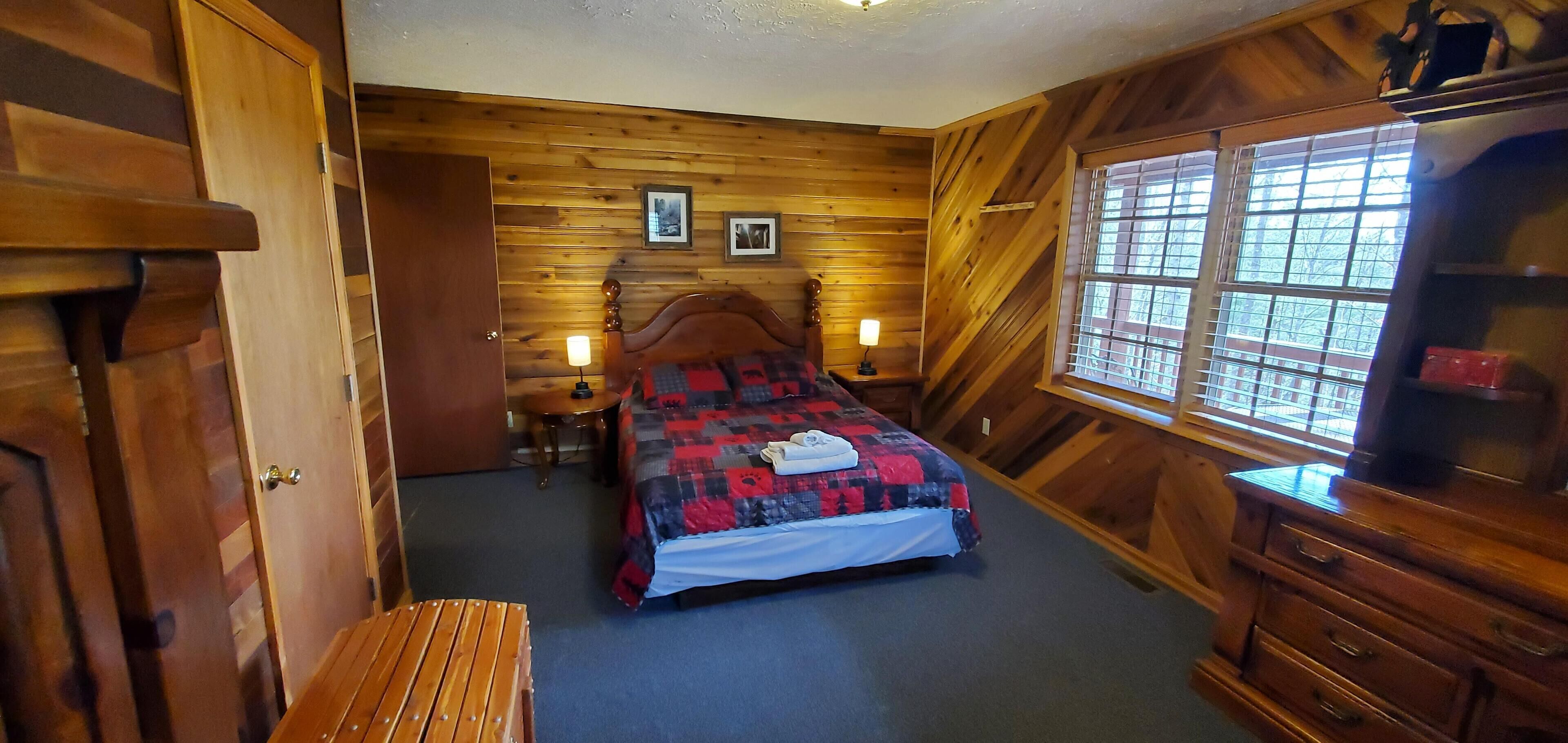 A wooden-paneled room with a bed, a desk, and a dresser.