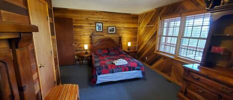 A wooden-paneled room with a bed, a desk, and a dresser.