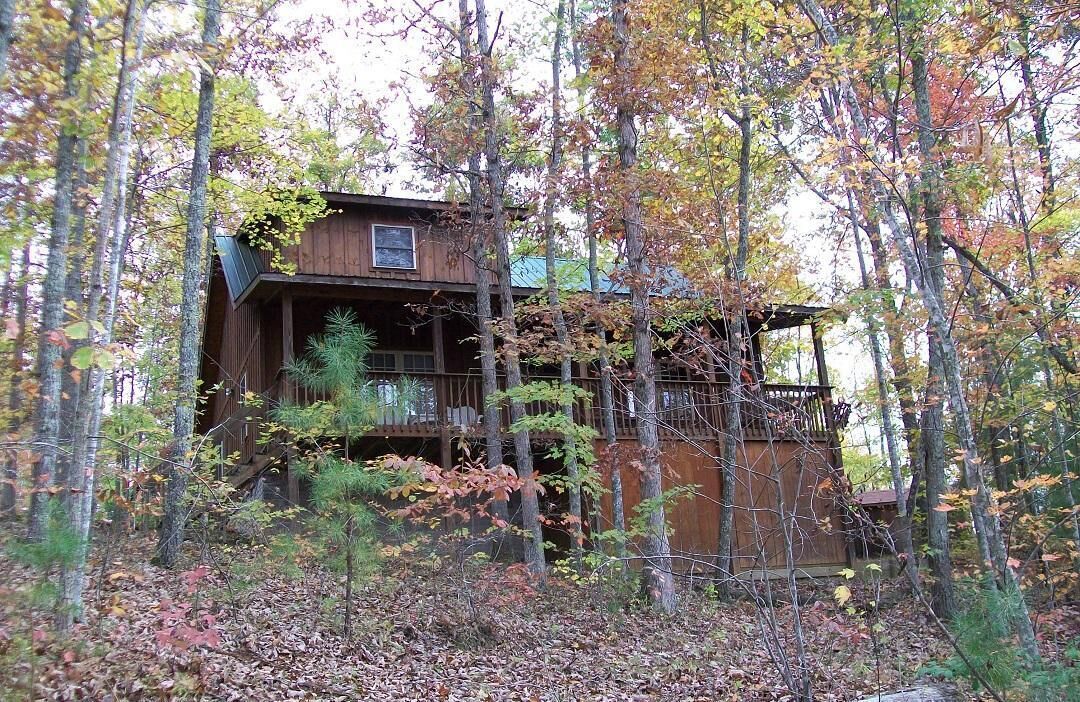 A cabin surrounded by trees with a wooden deck and a covered porch.