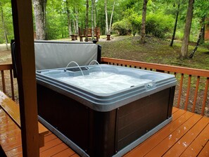 A hot tub on a wooden deck with a view of a forest.