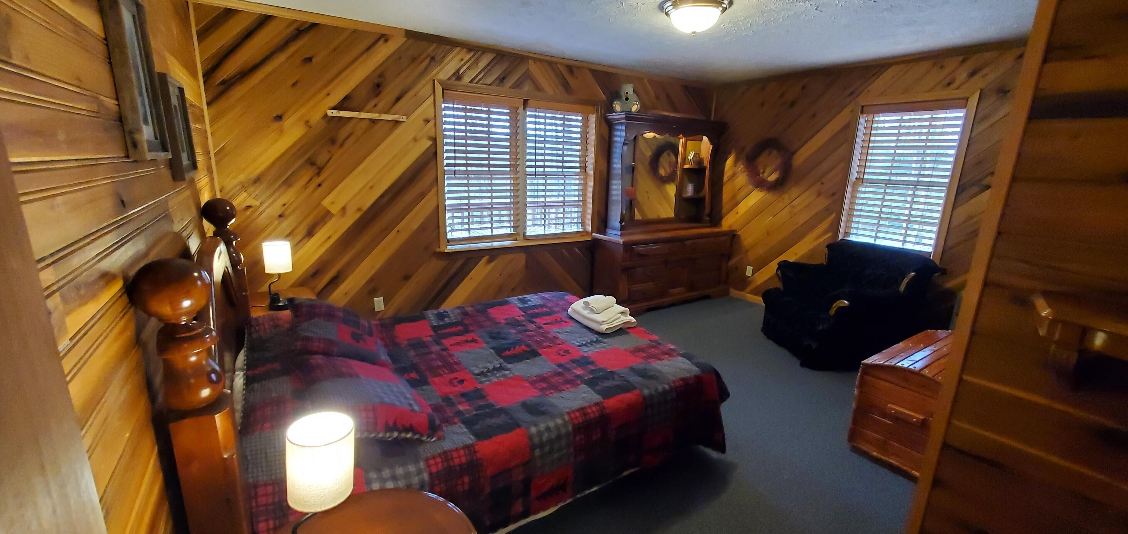 A cozy room with a bed, a dresser, a mirror, and two windows with blinds.