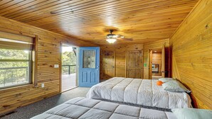 Una habitación con paredes de madera, ventilador de techo, dos camas, una puerta azul y una ventana.