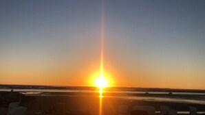 A beach scene with the sun setting over the horizon, creating a bright glare. - "kleine Antje" im Herzen von Butjadingen - Alles Parat für die Perfekte Auszeit! (Butjadingen)