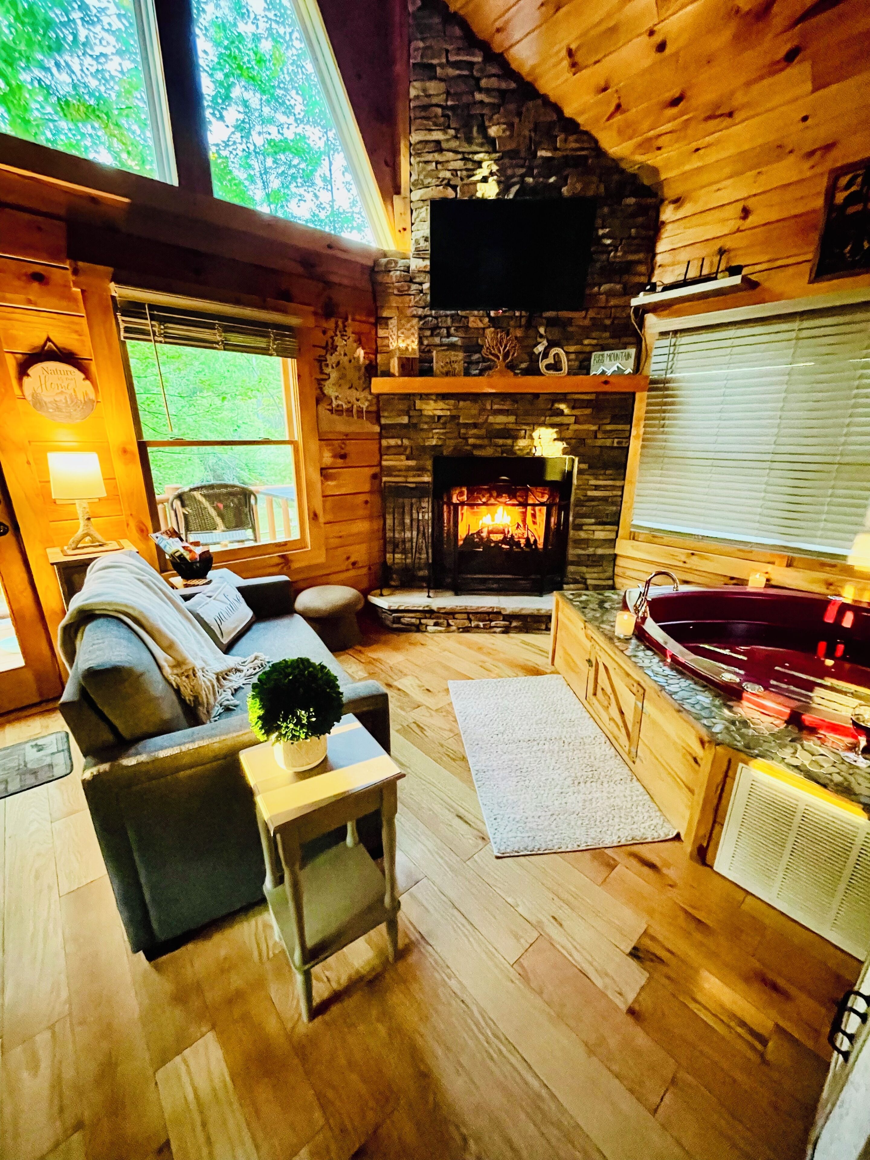 A cozy cabin interior with a fireplace, a sofa, a small table, and a hot tub.