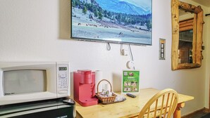 Une pièce avec un téléviseur diffusant un paysage enneigé, un four à micro-ondes blanc, une machine à café rouge, une table en bois et une chaise.