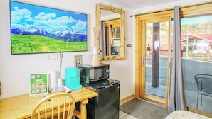Une chambre comprenant un lit, un bureau avec un ordinateur, un téléviseur diffusant un paysage de montagne, un four à micro-ondes et un réfrigérateur.