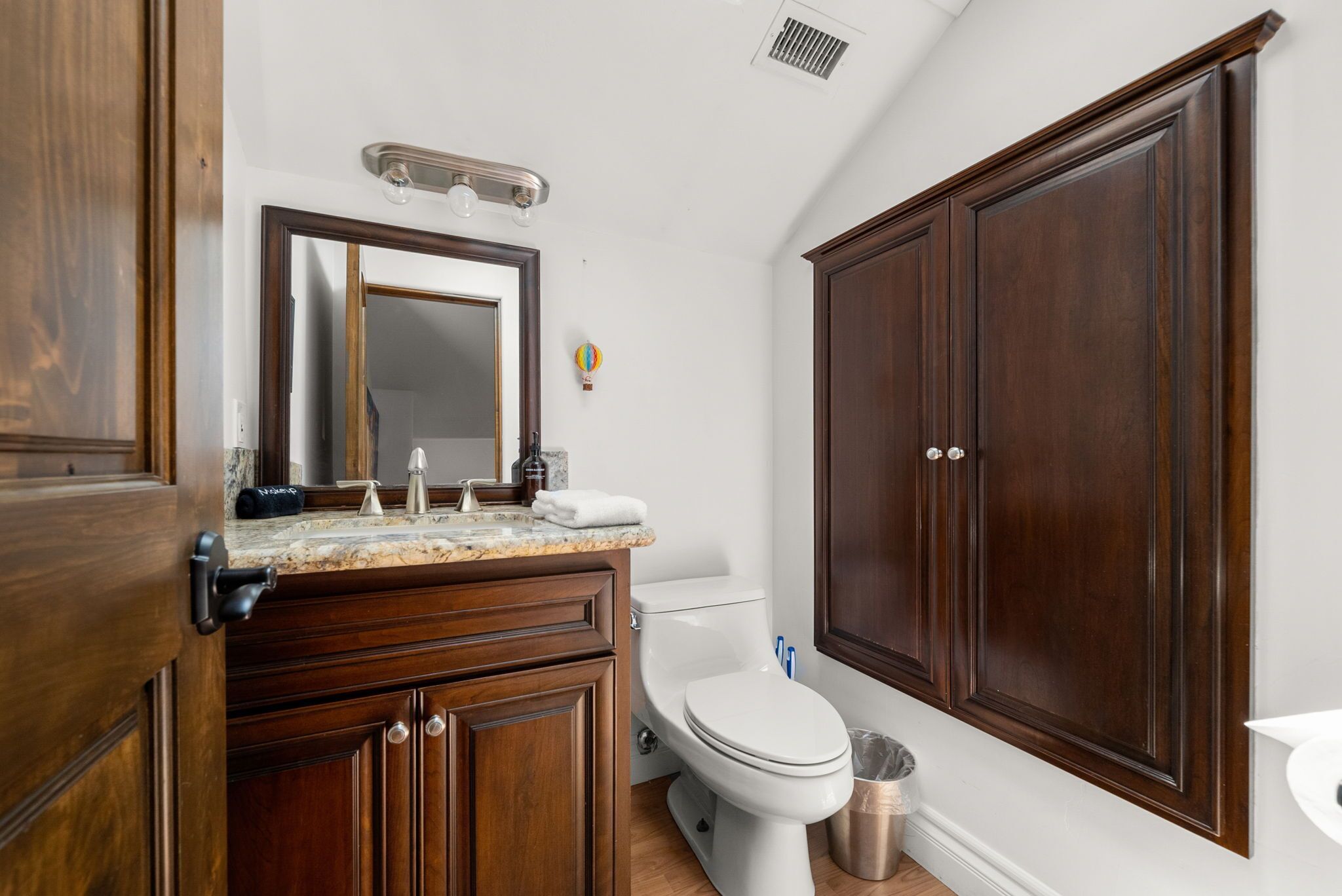 A bathroom with a wooden vanity, a toilet, and a large cabinet.