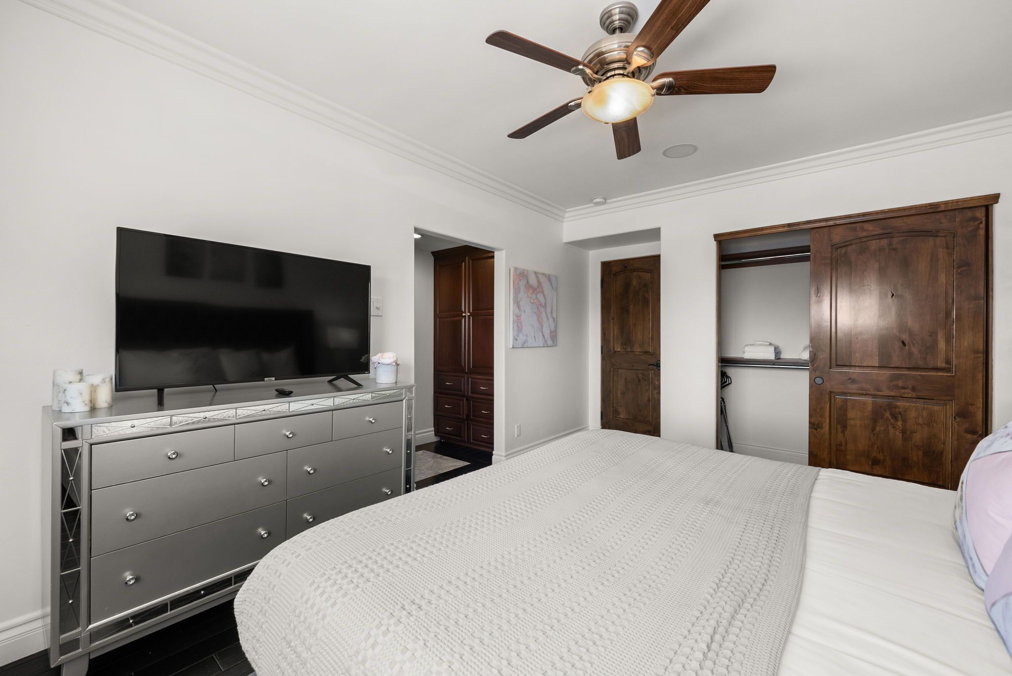 A bedroom with a large bed, a dresser, a television, and a ceiling fan.