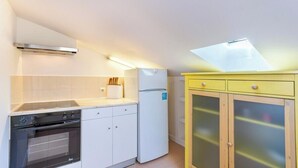 Une cuisine compacte dotée d’un four encastré, d’un réfrigérateur blanc et d’un meuble jaune aux portes en verre.