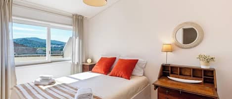 Ein Hotelzimmer mit Bett, Nachttisch, Lampe, Spiegel und Blick ins Freie.