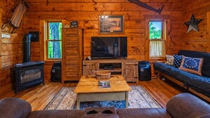 En mysig stuga med träpanel på väggarna, en öppen spis, en tv och en soffa.