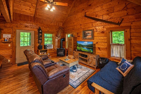 A cozy cabin interior with a fireplace, leather sofa, and a television.