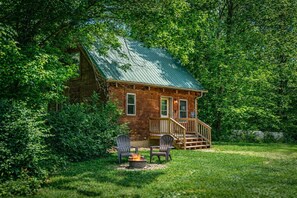 A rustic cabin with a porch, two chairs, and a fire pit.