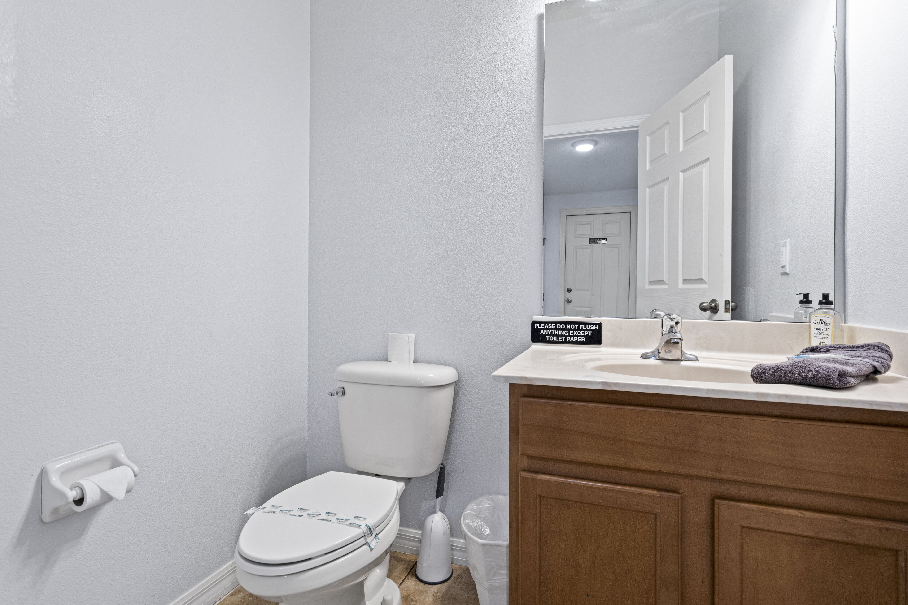 A bathroom with a toilet, sink, and mirror. A sign on the mirror instructs not to flush anything except toilet paper.