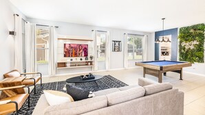 Una sala de estar moderna con mesa de billar, sofá, mesa de centro y televisor.