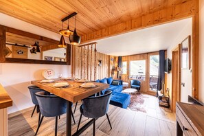 Een houten interieur met een eettafel gedekt voor vier personen, een blauwe bank en een skilift zichtbaar door het raam.