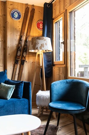 Een kamer met een houten inrichting, een blauwe bank, een stoel, een tafel en ski's die tegen de muur staan.