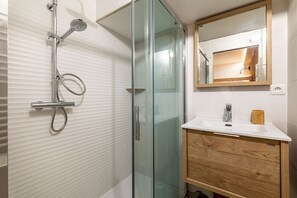Een moderne badkamer met een douchecabine van glas, een houten wastafelmeubel en een spiegel boven de wastafel.