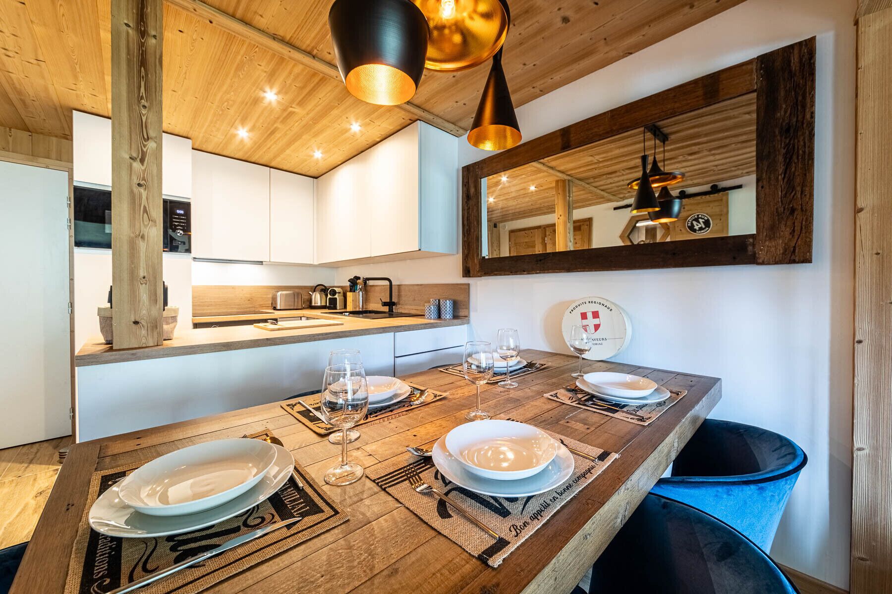 Een houten eettafel gedekt met borden, glazen en bestek, met een hanglamp en een spiegel aan de muur.