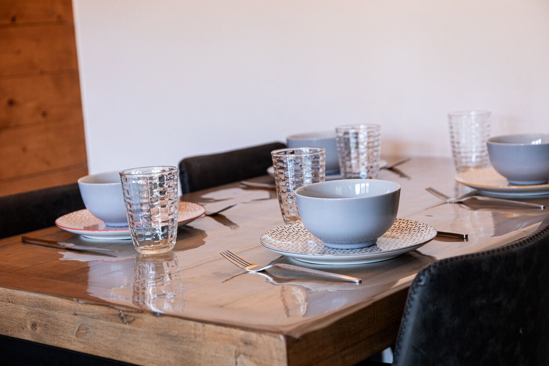 Une table à manger dressée avec de la vaisselle transparente et des bols bleus, agrémentée de couverts et de sets de table en fibres tressées.