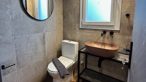 A bathroom with a toilet, a sink with a vessel basin, a mirror, and a window.
