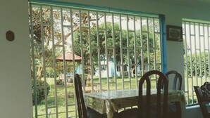 A dining area with a table and chairs, a view of a garden through barred windows, and a small gazebo in the background. - Room-habitación Y Baño Independientes (Jimenez)