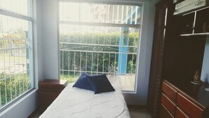 A room with a bed, a window with a view of greenery, and a wooden cabinet. - Room-habitación Y Baño Independientes (Jimenez)