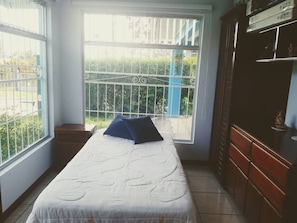 A room with a bed, a window with a view of greenery, and a wooden cabinet. - Room-habitación Y Baño Independientes (Jimenez)