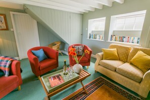 A cozy living room with a staircase, red and beige sofas, a coffee table with a magazine, and a bookshelf with books.