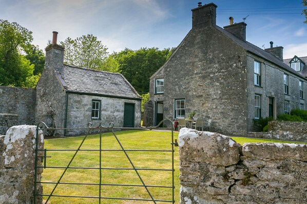 A stone building with a traditional design, featuring a large open yard and a metal gate.