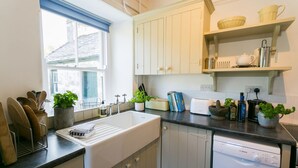 Et køkken med hvide skabe, opvaskemaskine og et vindue med blå persienner.