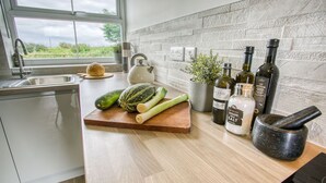 A kitchen with a wooden countertop, a white kettle, a cutting board with vegetables, a mortar and pestle, and bottles of olive oil. - Pen Y Parc Rhosneigr -  a coastal that sleeps 4 guests  in 2 bedrooms (Rhosneigr)