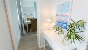 A hallway with a white console table, a lamp, and a poster of a coastal scene. - Pen Y Parc Rhosneigr -  a coastal that sleeps 4 guests  in 2 bedrooms (Rhosneigr)