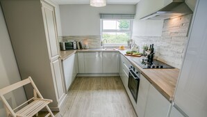 A modern kitchen with white cabinets, a wooden countertop, a built-in oven, and a window with a view of greenery. - Pen Y Parc Rhosneigr -  a coastal that sleeps 4 guests  in 2 bedrooms (Rhosneigr)