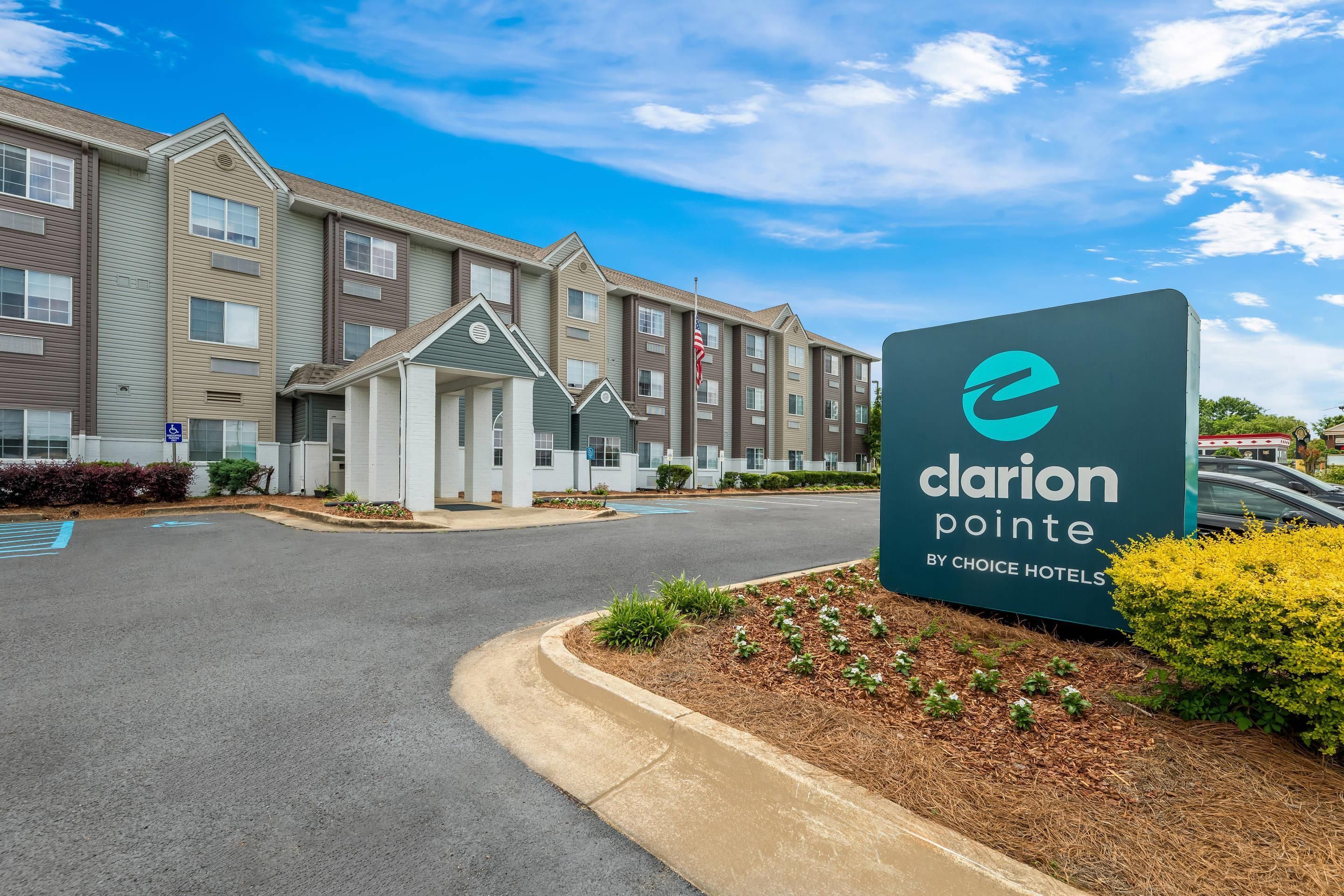A hotel entrance with a sign reading 'Clarion Pointe by Choice Hotels,' a driveway, and a parking lot.