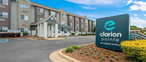 A hotel entrance with a sign reading 'Clarion Pointe by Choice Hotels,' a driveway, and a parking lot.