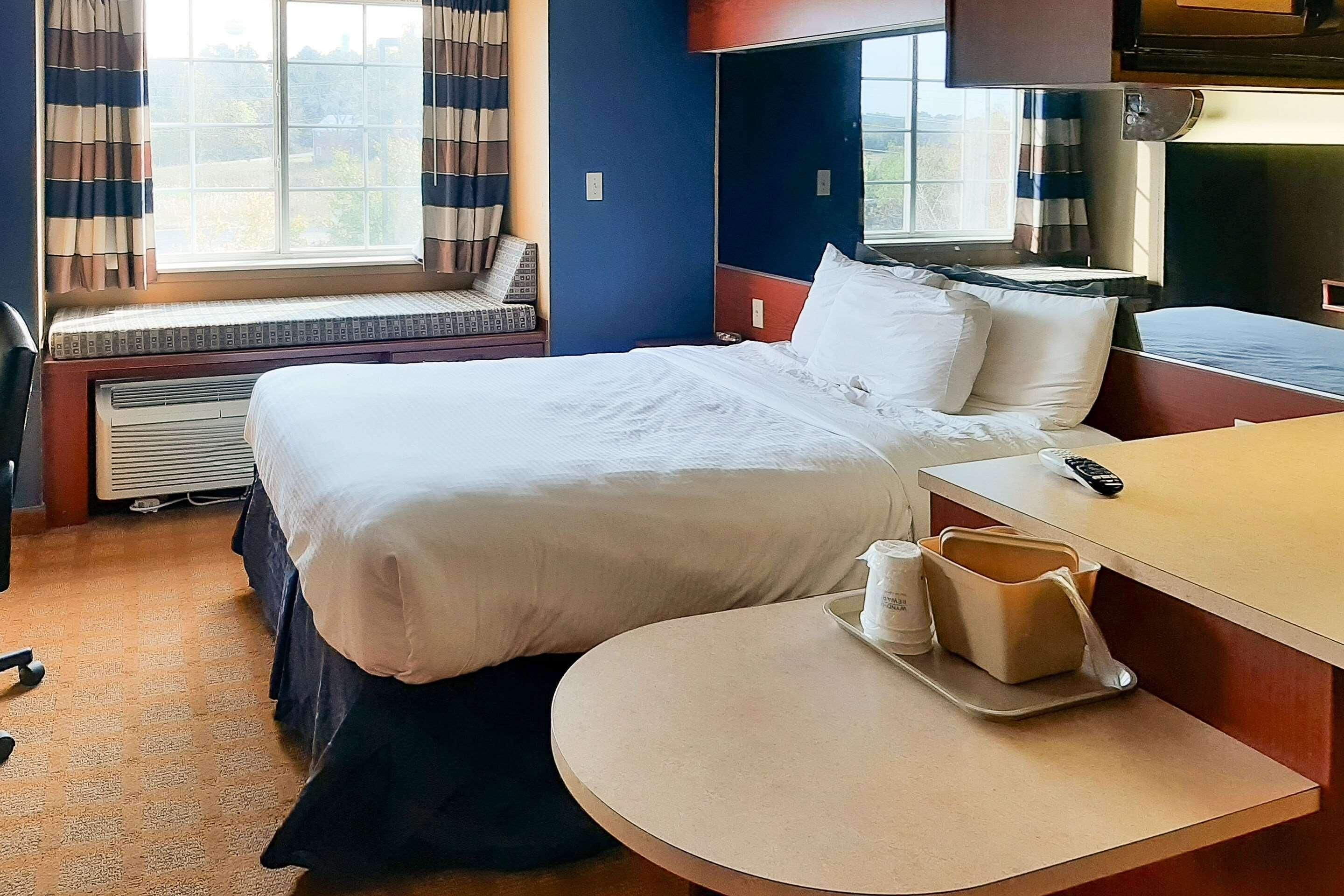 A hotel room with a bed, bedside table, and a window with curtains.
