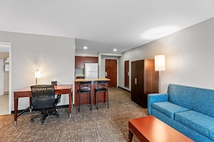 A hotel room with a desk, two chairs, a sofa, a small table, a kitchenette, and a wardrobe.
