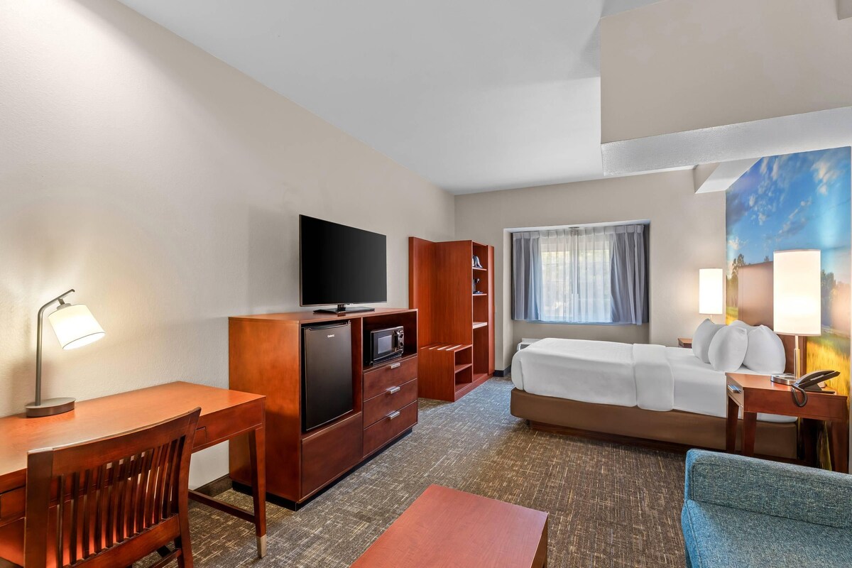 A hotel room with a bed, desk, TV, and a painting on the wall.