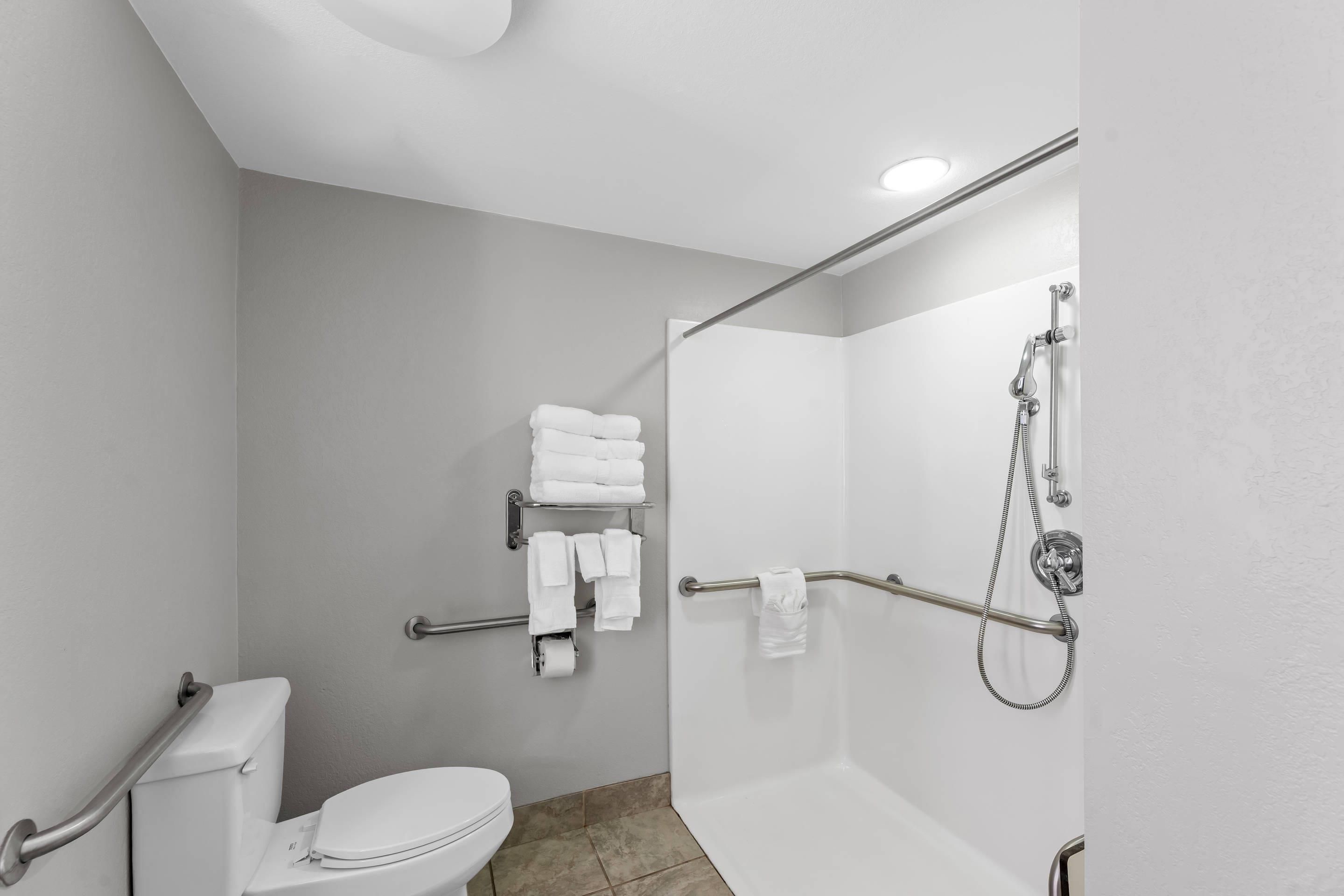 Un baño moderno con inodoro, ducha con barras de apoyo y toallero con toallas dobladas.